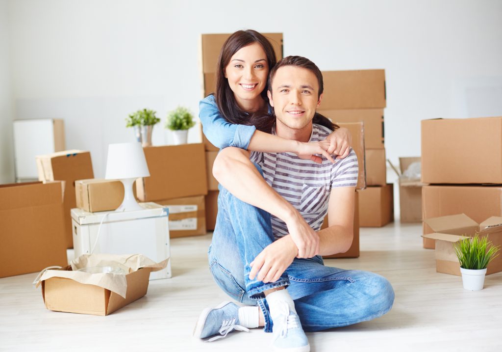 Happy young couple sitting on the floor of new house surrounded by boxes
